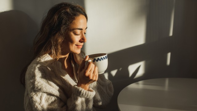 Article thumbnail: Morning ritual, sunrise awakening. Starting the day with cup of hot aroma coffee or tea. Breakfast pleasures. Coffee break. Attractive girl smiling and satisfact. Simple living
